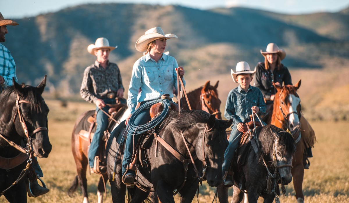 Happy big family enjoying horse riding together while using matching cowboy hats.