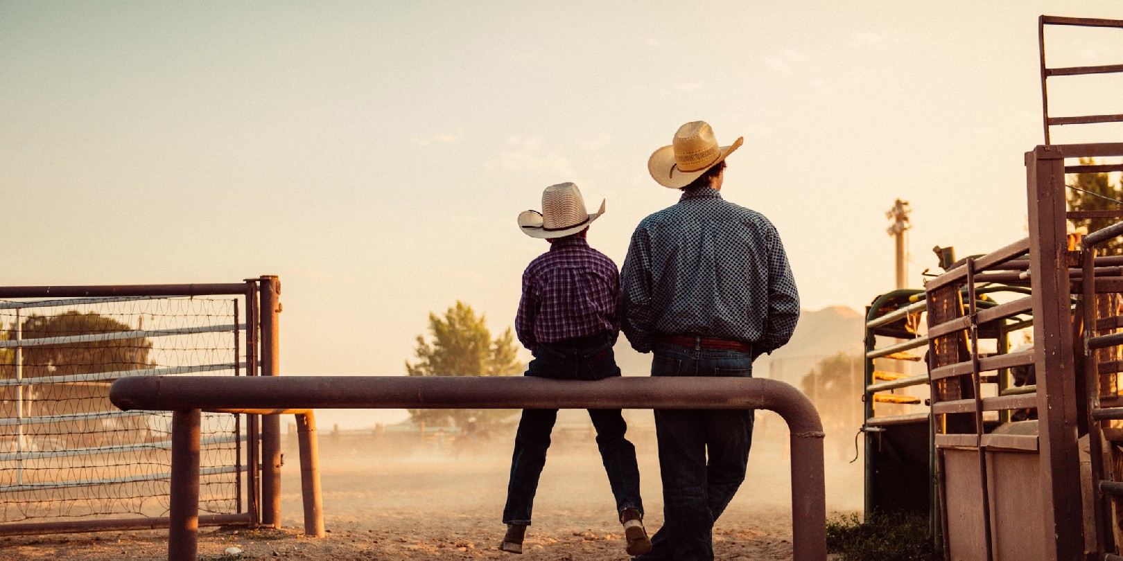 Father and son sitting by rodeo arena at sunrise