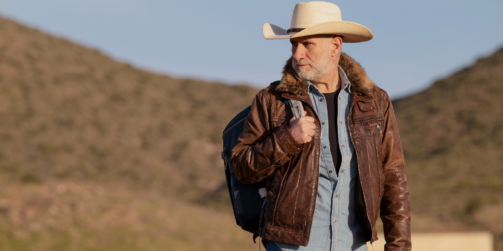 Adult man in cowboy hat standing on hill against mountain